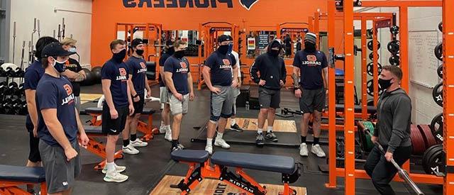 students learning from a coach in weight room